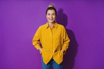 Young cheerful laughing girl wearing yellow shirt against purple background