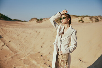 horizontal portrait of a woman in a light jacket and sunglasses, bag over her shoulder, posing against the backdrop of the desert