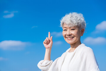 青空の下でオススメを指差すシニアの女性