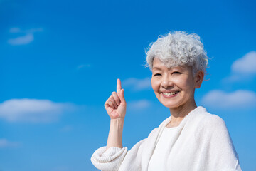 青空の下でオススメを指差すシニアの女性