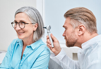 Otolaryngologist doctor checking mature woman's ear using otoscope or auriscope at ENT clinic....