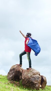 vertical shot girl with superman custume and enjoying by imagining at mountain - concept of childhood lifestyle, inspiration and adventure lifestyle