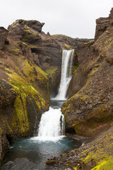 Obraz premium Waterfall flowing through mossy cliffs in Iceland's volcanic highlands.