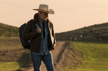 Adult man in cowboy hat on dirt road against sky