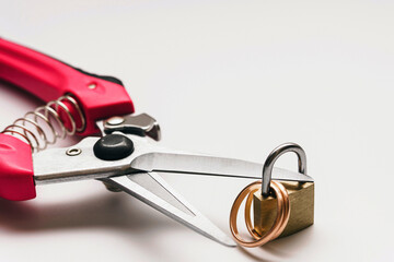 A macro photo of two golden rings locked on a padlock, while red handle nippers cutting the lock