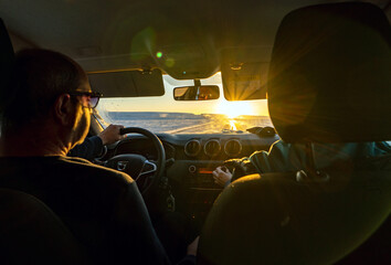 A middle-aged couple driving a 4x4 from inside the car at dawn on a totally snowy road with the sun rising over the horizon. © sirbouman