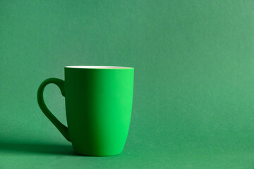 Green coffee or tea mug on green background. Space for text. Festive monochrome banner for design....