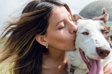 closeup of young latin woman of colombian ethnicity in the park kissing her dog on the face
