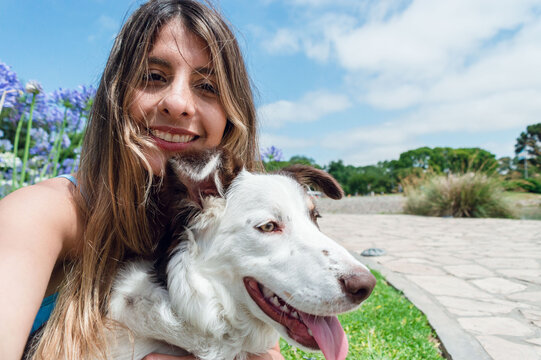 selfie portrait of young latin woman smiling with her dog sitting in the park, phone perspective
