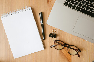 desktop top view, laptop, notepad, pen, glasses, paper clip, bank card, phone on a wooden table