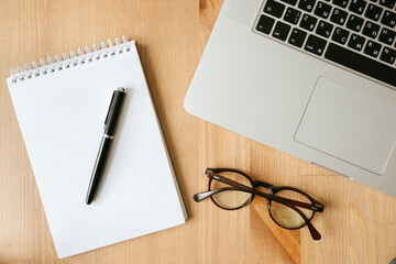 desktop top view, laptop, notepad, pen, glasses, paper clip, bank card, phone on a wooden table
