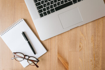 desktop top view, laptop, notepad, pen, glasses, paper clip, bank card, phone on a wooden table
