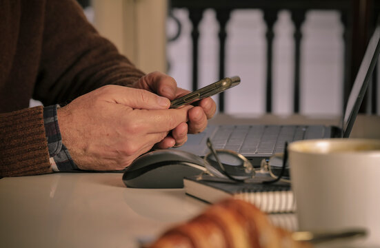 Closeup of adult man using smartphone in front of laptop