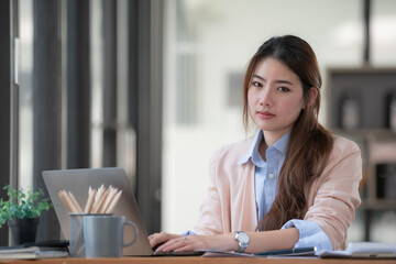 Portrait of a businesswoman using a laptop, smiling and looking at the camera while sitting at an office desk in a modern office.