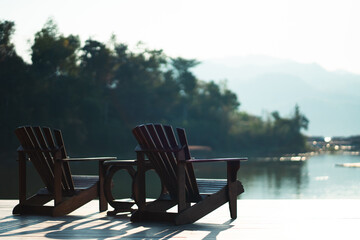 Fototapeta premium Classic wooden tables and chairs for relaxing by the resort's waterfront in the morning sunlight