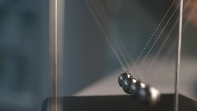 Man plays with newton cradle in room with blurry background closeup. Swinging steel spheres demonstrate physics law
