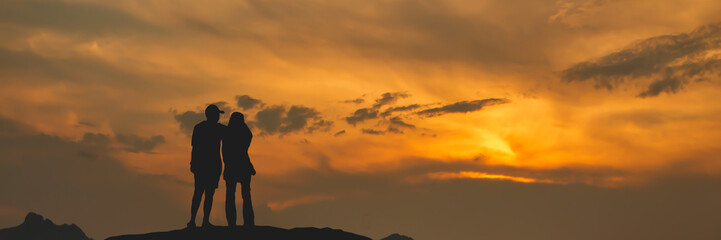 Silhouette of couple standing on top of mountain at dusk
