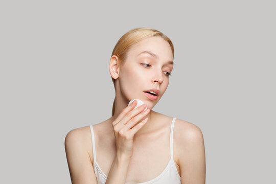 Portrait of beautiful woman doing her everyday routine removing her makeup with cotton pad on white background
