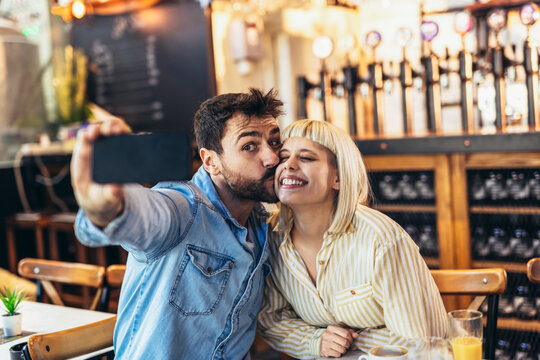 Young happy couple using smartphone to make selfie photo in cafe