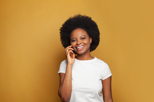 Happy young woman talking on the mobile phone and smiling against vivid yellow studio wall background