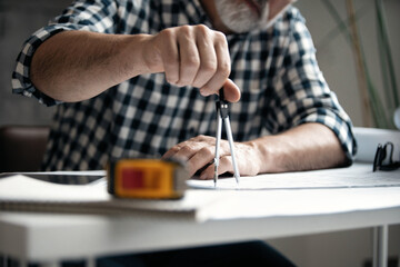 Obraz na płótnie Canvas Mature architect working on construction blueprint in modern office. Engineer using divider compass tools on blueprint