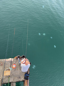 Fisherman with fishing rod in beautiful blue sea with jellyfish