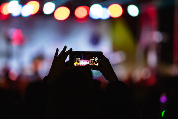 Fototapeta na wymiar Person holding smartphone and silhouettes of concert crowd with stage lights