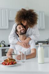 Fototapeta na wymiar curly young woman hugging cheerful boyfriend during breakfast.
