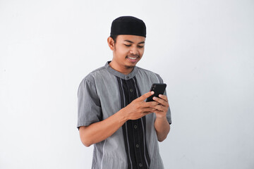 Happy or smiling young asian muslim man holding phone cellular wearing koko clothes isolated on...