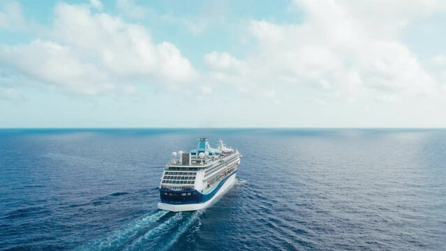 Orbit shot around large passenger cruise ship in sea at dramatic overcast weather with white clouds and blue sky.