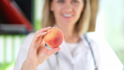 Happy doctor holds ripe reach in her hand.