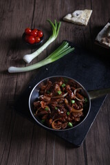 Beef meat stew in a pan and served with bread, green onion, and cherry tomato on a wooden table