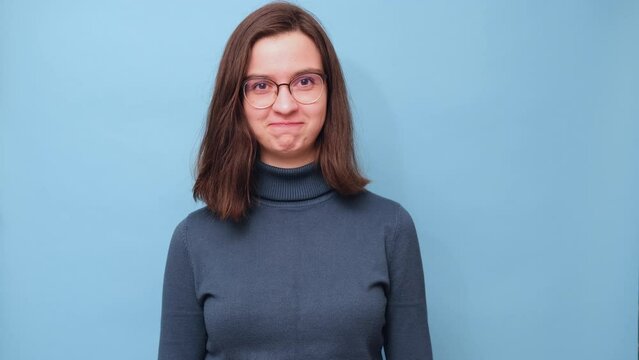 A smug smile. Portrait of a female student in glasses and a sweater with a smug smile on a blue background, 4K. emotion facial expression. feelings and people reaction.