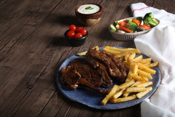 Grilled steak with french fries served with vegetables, cherry tomatoes, and garlic sauce on a plate on a wooden table