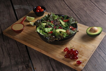 Healthy vegetable salad served on a wooden tray with avocado, grapes, lemon, cherry tomatoes, and dressing