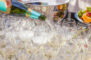 Row of glasses filled with champagne, someone holds bottle and fills in glasses. Bar counter. Banquet