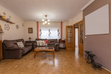 Living room furnished with somewhat kitschy decoration with wooden coffee tables and two twin corner sofas upholstered in brown fabric