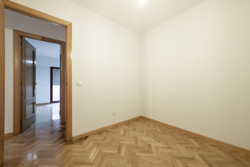 Small empty room with plain off-white painted walls, herringbone-shaped French oak parquet floors and doors of the same material