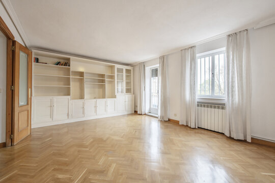 Empty living room with smooth white painted walls, French oak parquet floors laid in a herringbone pattern and custom-made white lacquered wooden bookcase