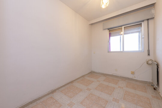 Small empty room with plain white painted walls, ugly tiled floor and double aluminum window
