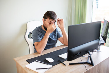 Tired male programmer rubbing his nose and eyes because of weariness in the office. Concept:...