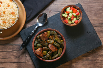 Egyptian okra casserole served with lemon, salad, and Egyptian rice with tahini and garlic on a black tray