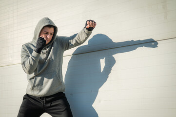 A man in a hoody trains boxing against a gray wall.  - Powered by Adobe