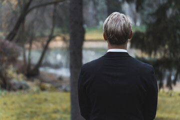 Back view of an blonde handsome man in suit in a forest. High quality photo