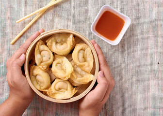 Clutching a bamboo bowl with dim sum, chopsticks and red sauce, top view
