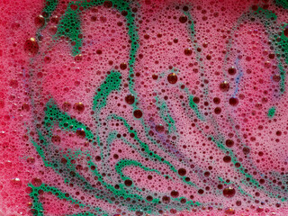 Pink foam with green veined, marbled pattern of dissolve aromatic bath bomb in water.