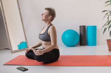 short hair blonde in a black short top and leggings is doing yoga on a mat. A girl with a little extra weight and folds at the waist is doing Pilates and plank. Body positivity and self acceptance