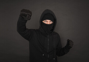 Man in the black hoody with hood wearing balaclava mask with fist up