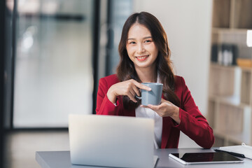 Adorable businesswoman holding coffee cup while working in the office room.