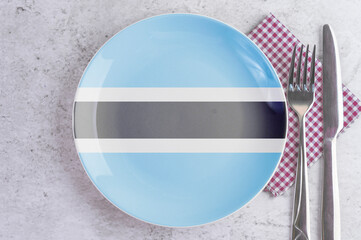 A Plate with the Flag of Botswana, Cutlery and Napkins on the Mable Table.